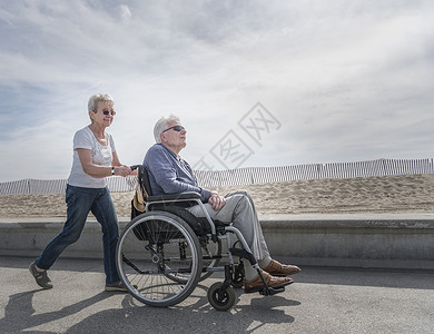 海滩上老年妇女在推着丈夫的轮椅图片