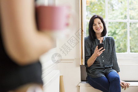 创意工作室窗边座位上拿着手机微笑的女设计师背景图片