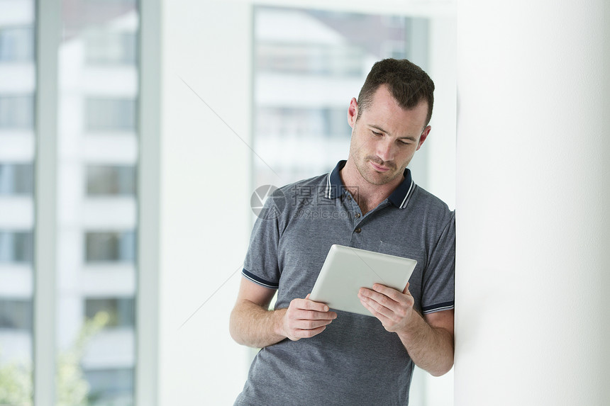 靠在墙上看数字平板电脑的男士图片