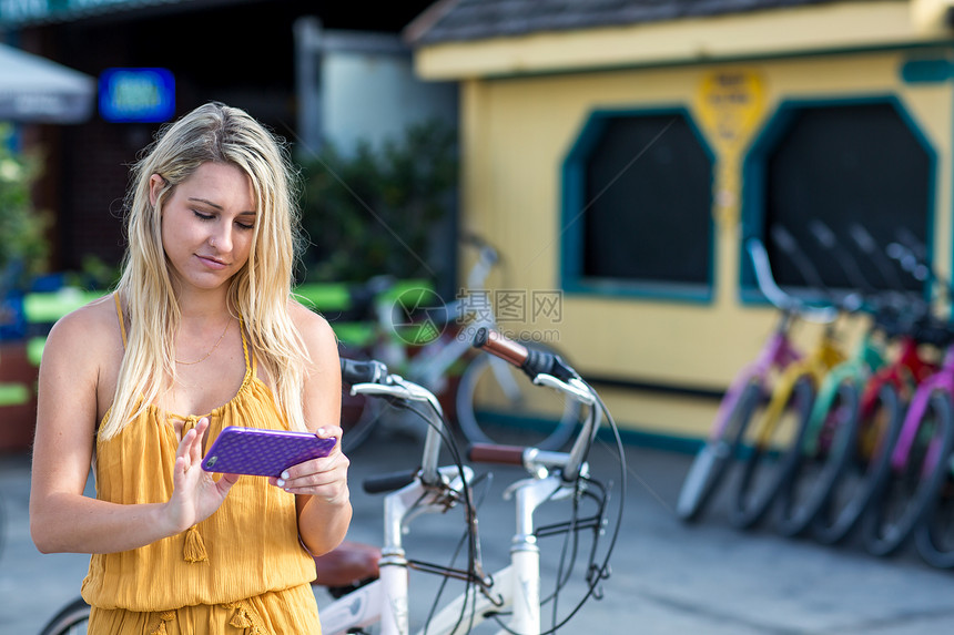 美国加利福尼亚州圣莫尼卡一位金发女郎骑自行车看智能手机图片