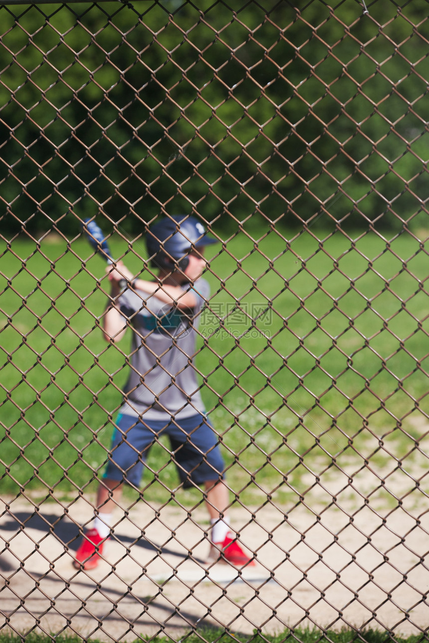 透过鸡铁丝网查看打棒球的男孩图片