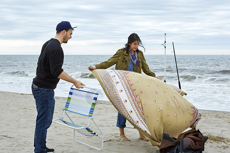 在海滩上准备沙椅和野餐毯子的年轻海鱼夫妇图片