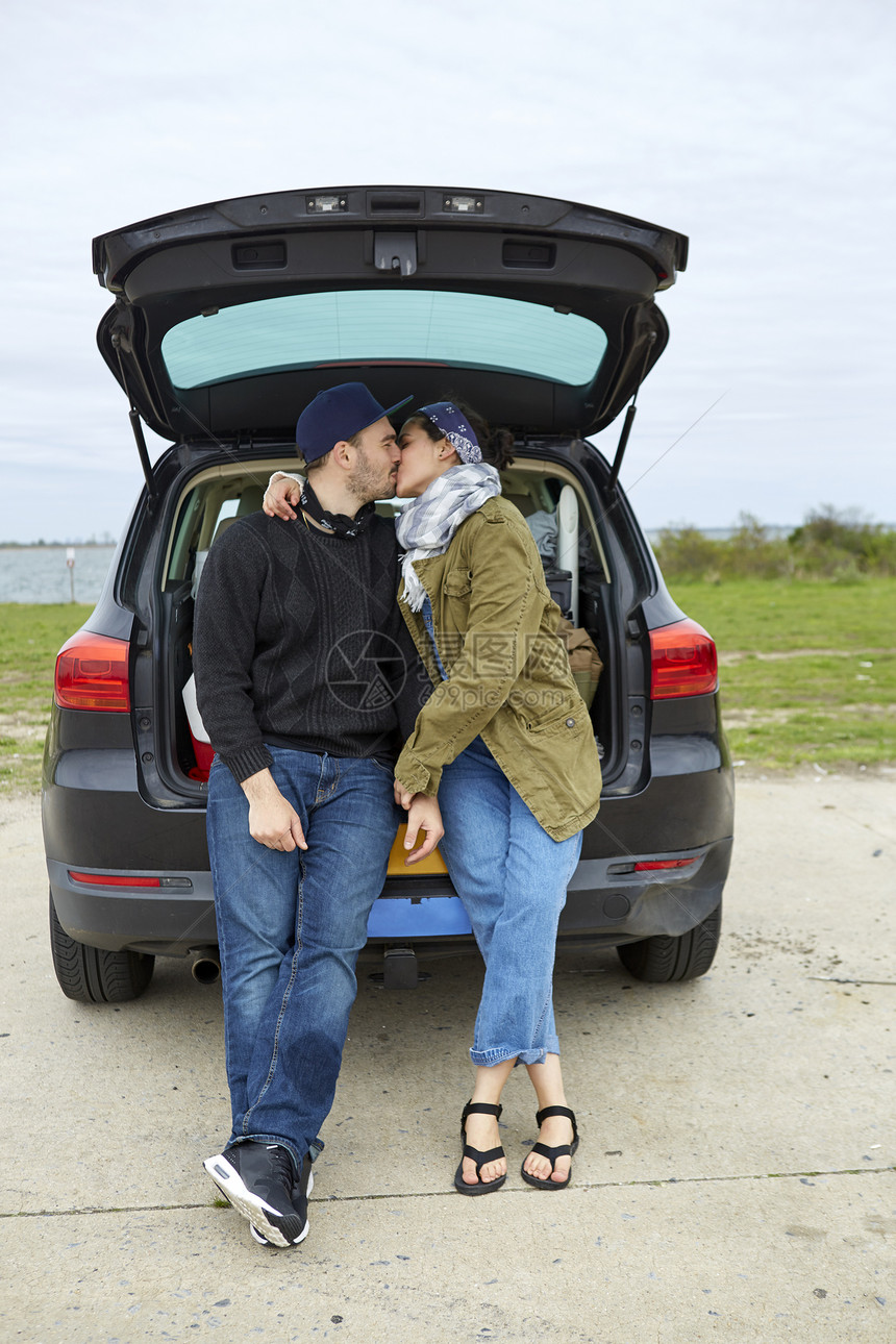 年轻夫妇坐在敞开的着的汽车后备箱上亲吻图片