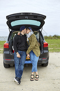 年轻夫妇坐在敞开的着的汽车后备箱上亲吻图片