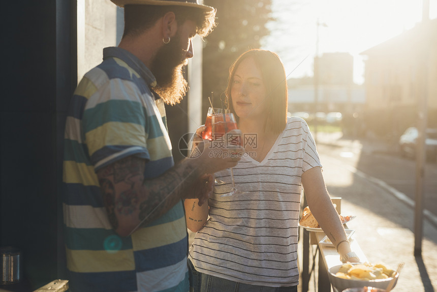 一对夫妇在日光落的人行咖啡厅举杯鸡尾酒图片