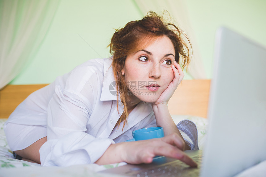 使用笔记本电脑在床上跪的年轻妇女图片