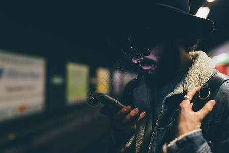 年轻人站在地铁平台上看着智能手机图片