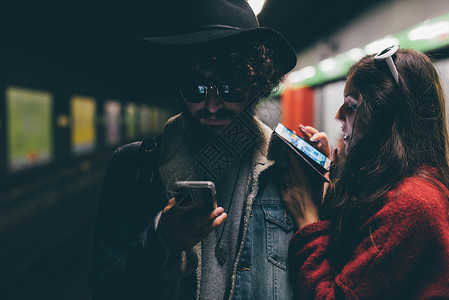 坐在地铁平台上看智能手机的年轻夫妇图片