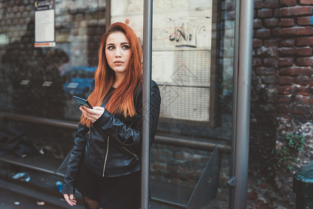 红发女子在巴士站等候时拿着智能手机图片