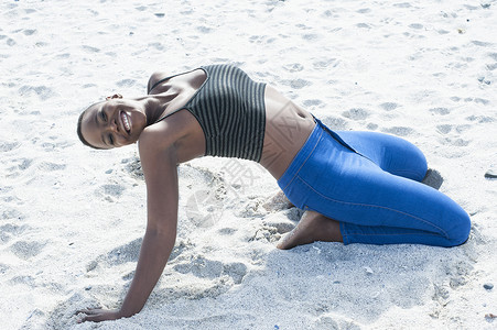 年轻女子跪在沙滩上向后伸展图片