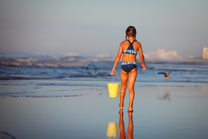 海滩上拎着水桶的女孩的背影图片