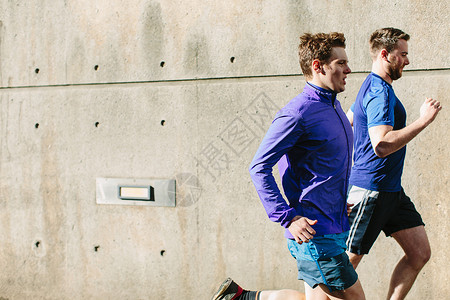 两名年轻的男跑步者沿着城市人行道跑图片