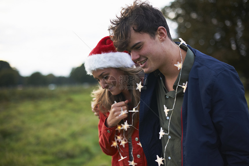 一对戴着圣诞帽和圣诞花环的年轻夫妇在田野里漫步图片