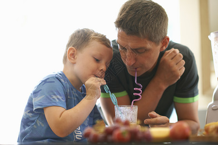 男孩和父亲在厨房里共享新鲜的水果汁图片