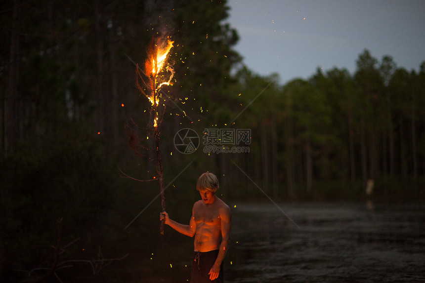 青年男子站在水边黄昏时分拿着烧焦的树枝图片