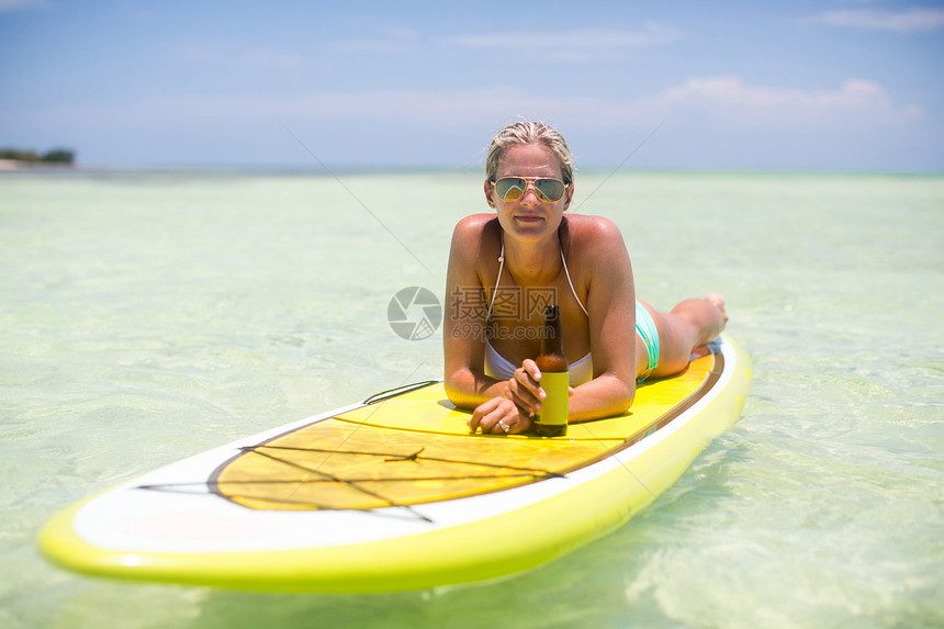 中年成女子在冲浪板上放松拿着一瓶啤酒图片