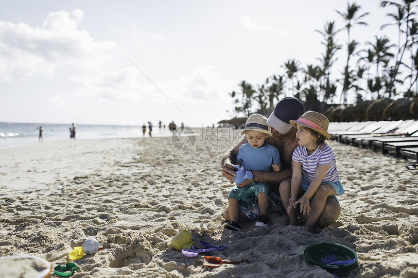 父亲坐在沙滩上与小儿子和女坐在一起图片