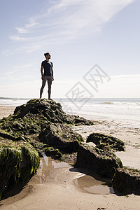 从海滩岩石向外看的年轻男子图片