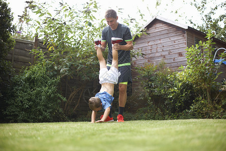 花园里父亲抬着儿子的腿帮他倒立高清图片