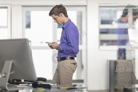 在办公室里看智能手机的年轻男办公室工人图片