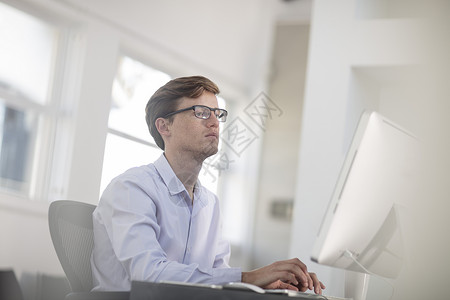 年轻男办公室职员在台式电脑前打字图片