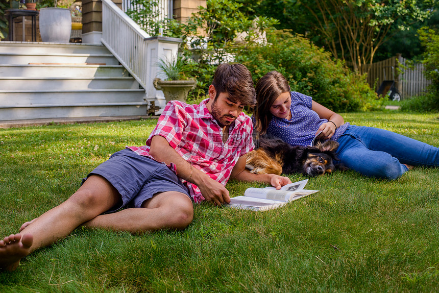 一对夫妇躺在花园的草地上与狗阅读图片
