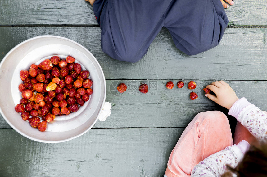 两个孩子坐在木地板上旁边放一碗草莓图片
