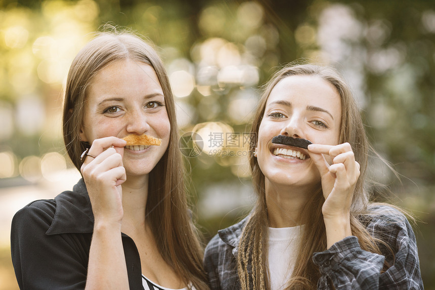 公园里两位年轻女人用叶子假扮胡子微笑图片