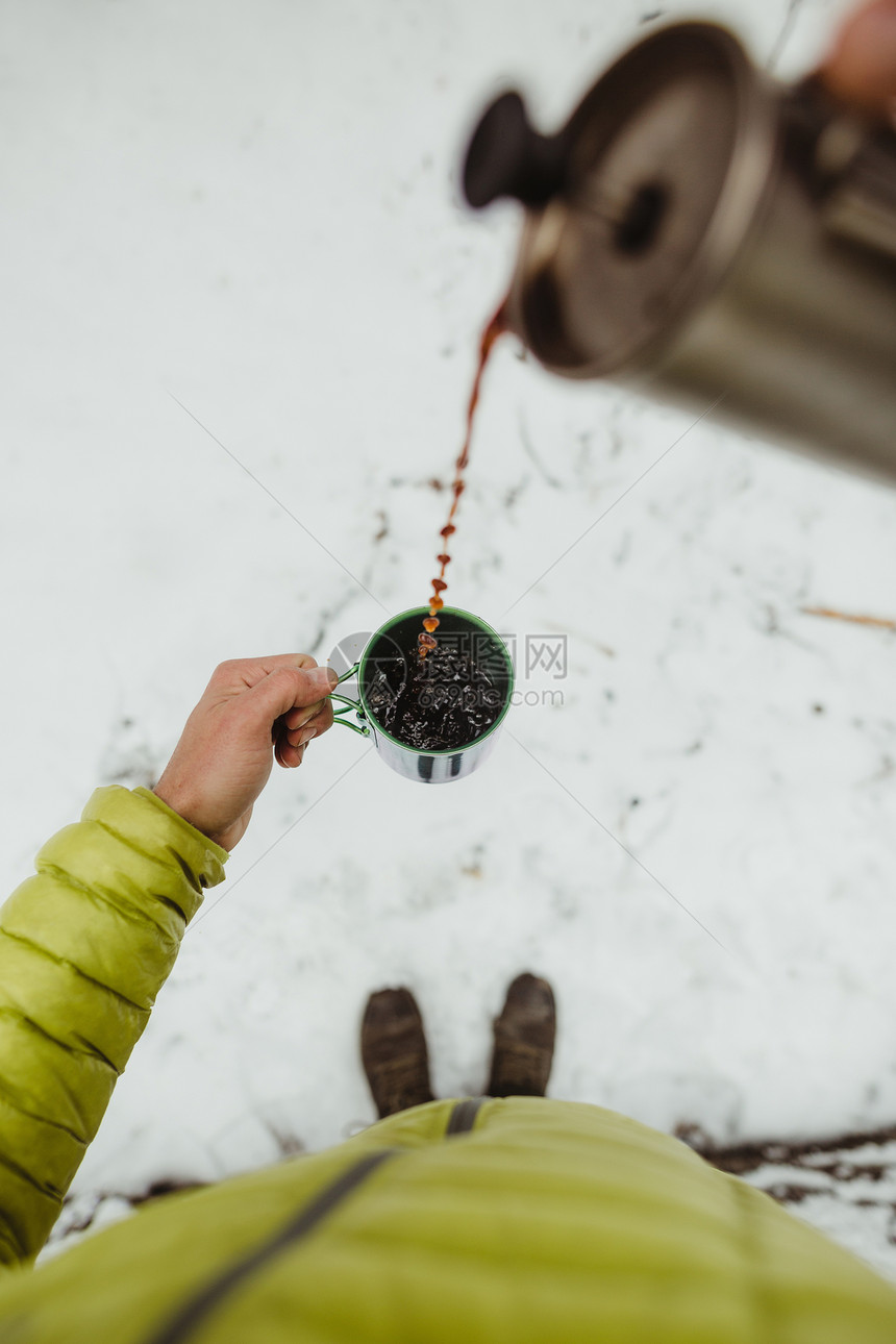 男徒步旅行者站在雪地上倒咖啡的手图片