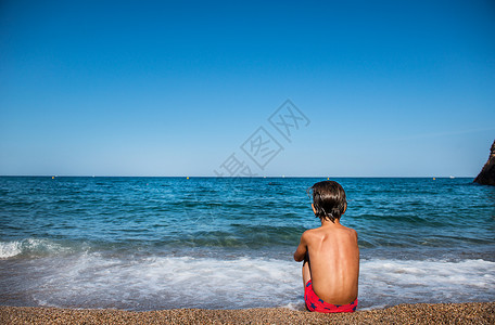 坐在海滩上眺望大海的男孩图片