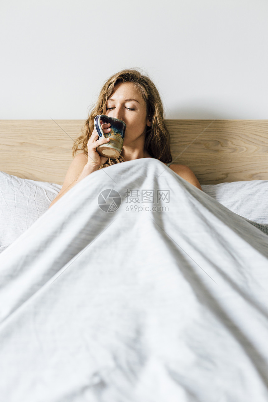 坐在床上喝着咖啡的年轻女士图片