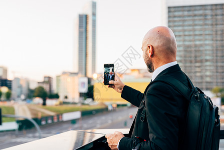 成熟的商人站在户外用智能手机自拍图片