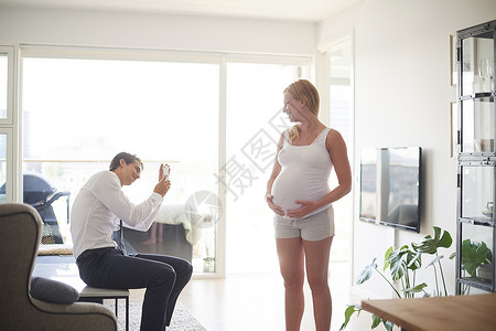 男人在客厅用手机拍怀孕女友的照片图片