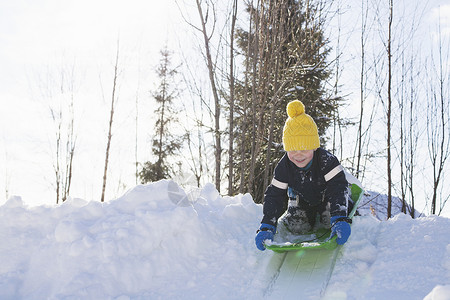 戴着黄色针织帽的男孩在白雪覆盖的小山上滑雪高清图片