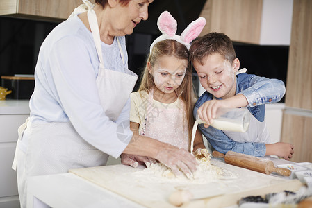 女孩和兄弟在厨房柜台帮助祖母复活节烧烤图片