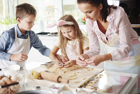 在厨房柜台烤东西饼干的女孩兄弟和母亲图片