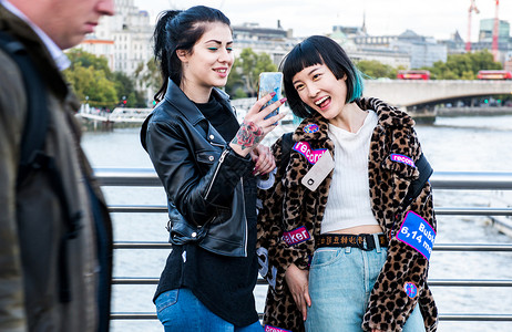 两位年轻时尚女在千禧桥上笑着看手机图片