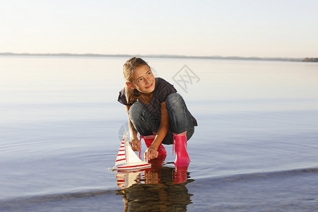 女孩在水上玩漂浮的玩具船背景图片