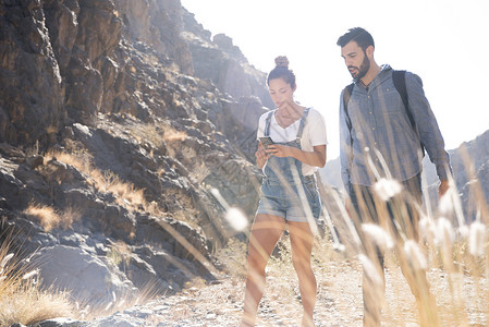 在西班牙加那利群岛拉斯帕尔马山谷旅行时看着智能手机的年轻徒步夫妇图片