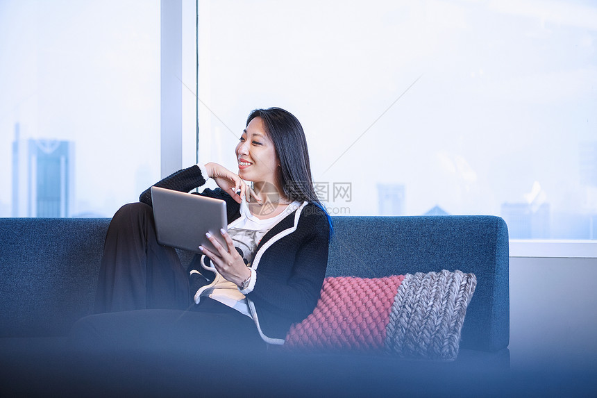 沙发上的妇女笑着使用数字平板电脑图片