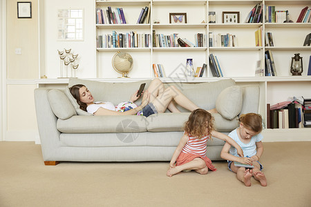孕妇靠在沙发上女儿坐在地板上玩智能手机图片