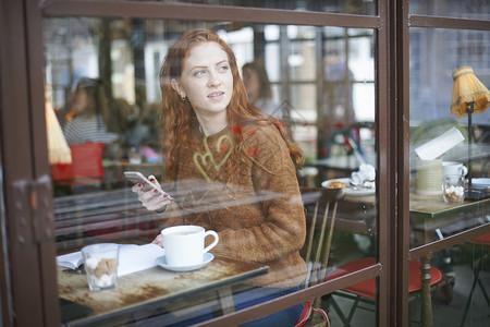 在咖啡店拿着手机透过窗户看外面的女人图片