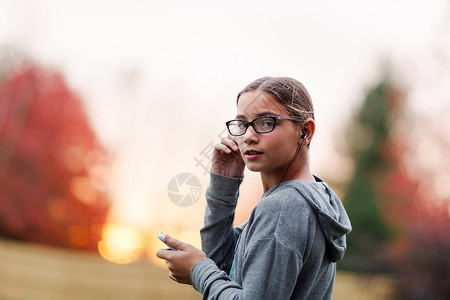 坐在花园的肩膀上看着听智能耳机音乐的女孩肖像图片