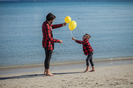 父亲和儿子在海滩上拿着两个黄色气球图片