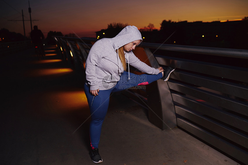 经济的年轻妇女培训夜间在人行桥上触摸脚趾图片