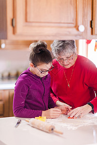 油酥面团女孩和祖母在厨房柜台用饼干模具切面团背景