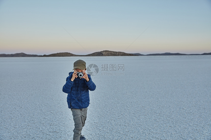 青年男孩站在盐滩上拿着相机拍照图片