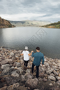 在美国科罗拉多州湖边岩石上手牵手行走的情侣图片