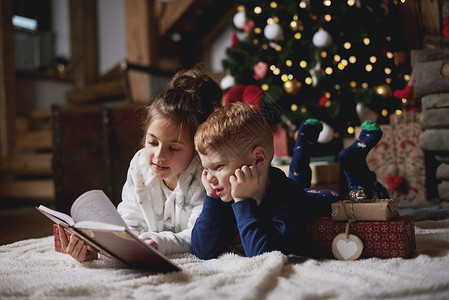 女孩和男孩在圣诞树旁边看书图片