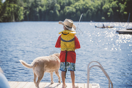 牛仔帽男孩和狗在湖边码头钓鱼高清图片